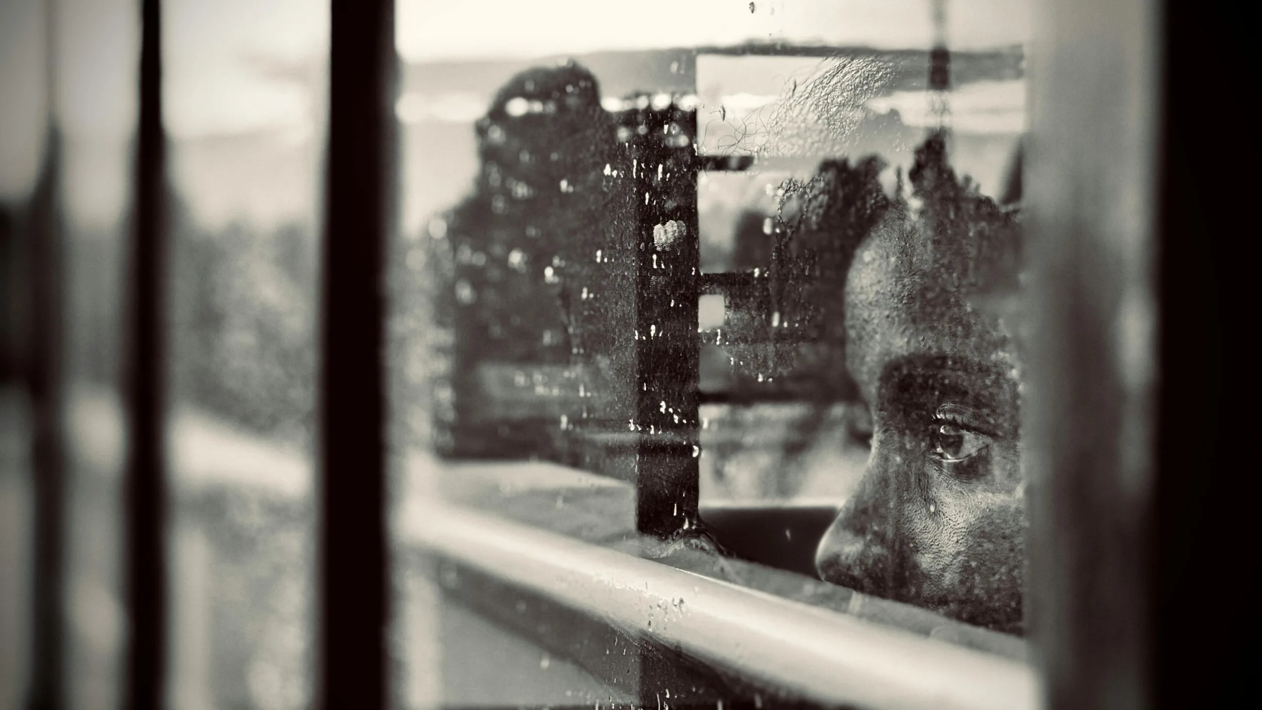 Person looking through a rain-covered window, reflecting feelings of anxiety, hypervigilance, overthinking, and emotional isolation.
